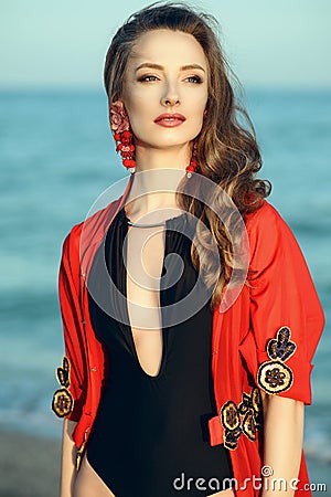 Beautiful woman standing at the seaside wearing trendy one piece halter neck swimsuit and red oriental beach cover up Stock Photo