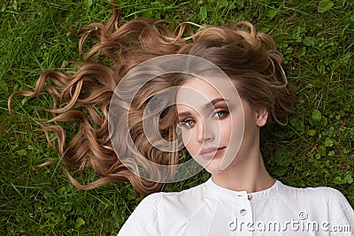 Beautiful woman with long healthy curly blonde hair relaxing on green grass outdoors Stock Photo