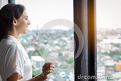Beautiful woman look at nice view of cityscape at condominium room or hotel of hig building. Gorgeous woman wear bathrobe. Pretty Stock Photo
