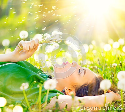 Beautiful woman lying on the field in green grass and blowing dandelion Stock Photo