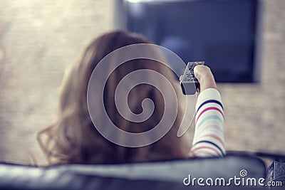 Beautiful woman lying on a sofa with remote control and watching television Stock Photo