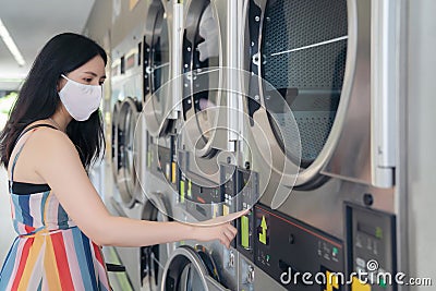 Beautiful woman with mask doing laundry at laundromat shop Stock Photo