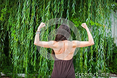 Beautiful woman with naked back over green weeping willow background. Sport girl shows back muscles. Stock Photo