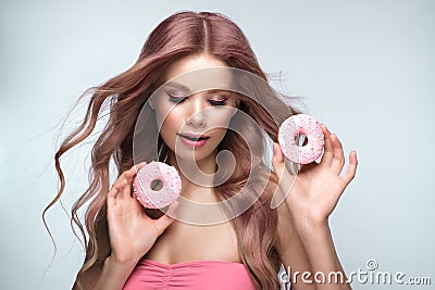 Beautiful woman with pink hair, beautiful makeup with donuts in her hands posing in the studio. Stock Photo