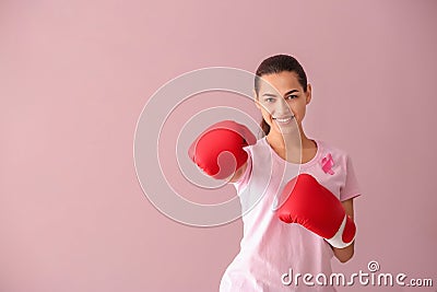 Beautiful woman with pink ribbon and boxing gloves on color background. Breast cancer concept Stock Photo