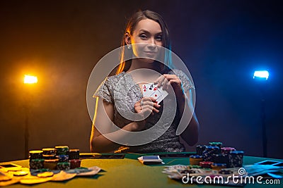 Beautiful woman playing in casino, look at camera and shows her cards. Lucky player on smoky background with lamps. Concept of Stock Photo