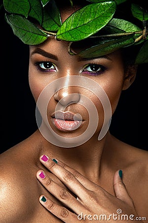 Beautiful woman portrait on black background. Young afro girl posing with green leaves. Gorgeous make up. Stock Photo