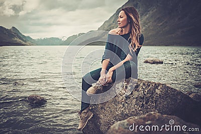 Beautiful woman posing on the shore of a wild lake, with mountains on the background. Stock Photo