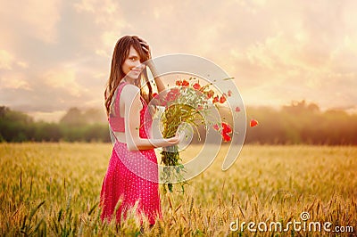 Beautiful woman in a red dress with a bouquet of poppies in a wheat field at sunset, warm toning, happiness and a healthy lifestyl Stock Photo