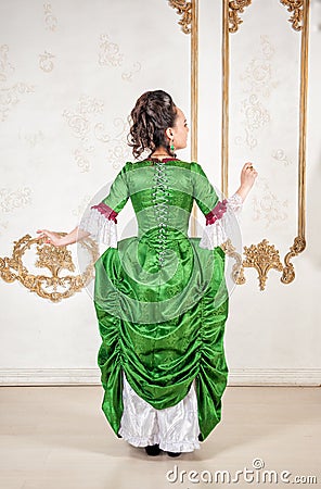Beautiful woman in rococo style medieval dress standing near wall back pose Stock Photo
