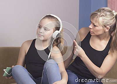 Beautiful woman is scolding her teenage daughter, girl is listening to music in headphones and ignoring her mom Stock Photo