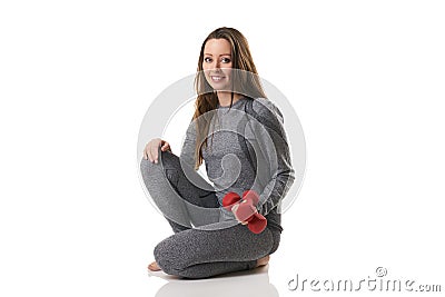 Beautiful woman in sitting position keeping two red dumbbells in one hand in gray thermal underwear. Stock Photo