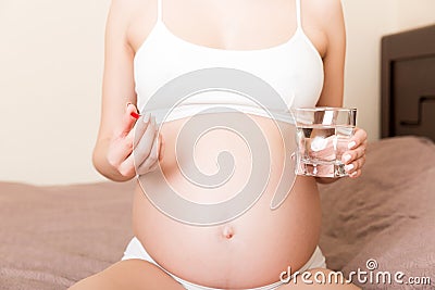 Beautiful woman sitting on sofa holding a pill and water Stock Photo