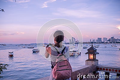 Beautiful woman standing taking a photo of sunset. Happy young woman with a camera and a backpack. Stock Photo