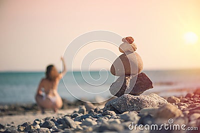 Beautiful woman in a swimsuit walking along the beach against the background of a pyramid of stones. Blurred female with stones on Stock Photo