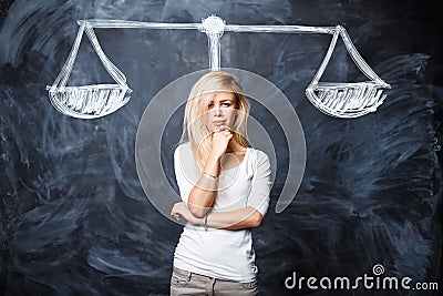 Beautiful woman is thinking, weighing the situation, making a choice in the studio near a chalk board with drawn scales Stock Photo