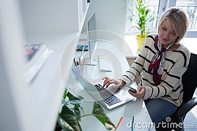 Woman using mobile phone and laptop at table Stock Photo