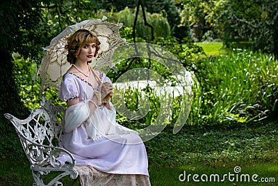 Beautiful woman in vintage dress sitting on ornate metal bench holding parasol next to river Stock Photo