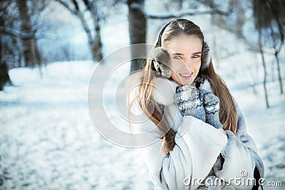 Beautiful woman walking in earmuff, knitted mittens and fur coat have fun in winter forest Stock Photo