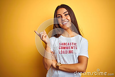 Beautiful woman wearing fanny t-shirt with irony comments over isolated yellow background with a big smile on face, pointing with Stock Photo