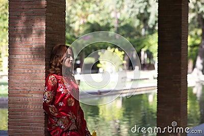 A beautiful woman wears a traditional Moroccan dress in red and embroidered in gold and silver. The beautiful woman is leaning on Stock Photo