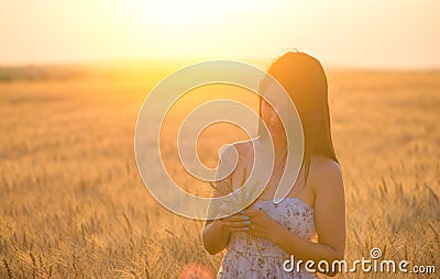 Beautiful woman with a wheat bouguet in wheat field at sunset Stock Photo