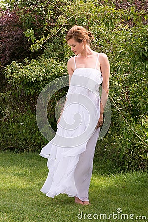 Beautiful woman in a white dress standing barefoot on the grass. Stock Photo