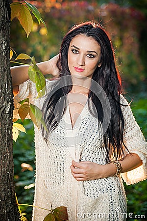 Beautiful woman in white posing in autumnal park. Young brunette woman spending time in autumn near a tree in forest Stock Photo