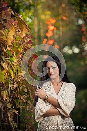 Beautiful woman in white posing in autumnal park. Young brunette woman spending time in autumn near a tree in forest Stock Photo