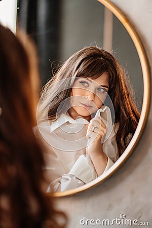 a beautiful woman in a white shirt looks at her reflection in a round mirror. Stock Photo