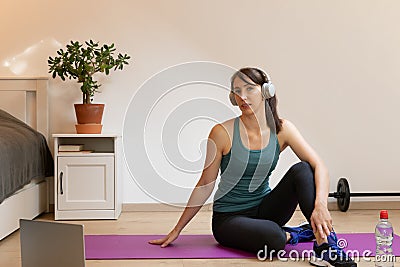 Beautiful women doing fitness at home near bed and watching online tutorials on laptop in natural light. Sport and recreation Stock Photo