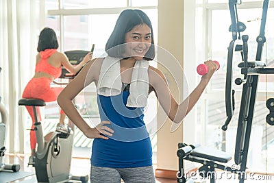 Woman wearing blue and gray sportswear while holding dumbbells. fitness slim young woman lifting weights in gym. Stock Photo