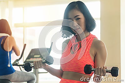 Woman wearing orange sportswear while holding dumbbells looking at camera. Fitness slim young woman lifting weights in Stock Photo