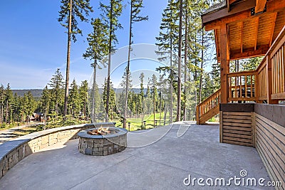 Beautiful wooden back porch with chairs on the hill and large backyard patio with fire pit and pine trees Stock Photo