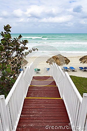 Beautiful wooden ladder to the ocean beach. Beach with straw umbrellas and sun-loungers. Cloudy sky and blue water Stock Photo