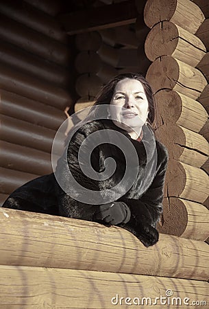 A beautiful 45-year-old woman with red hair poses on the veranda of a log house. Stock Photo