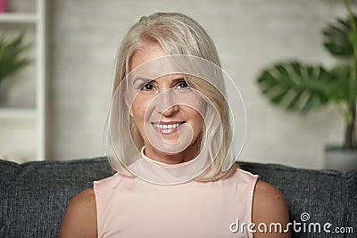 Beautiful 50 years blonde woman is smiling sitting on a sofa at home Stock Photo