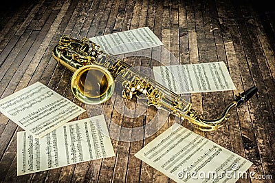 beautiful yellow saxophone and paper with music score notes lying on a vintage wooden stage Stock Photo