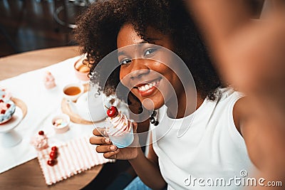 African blogger presenting cupcake with selfie on smartphone. Tastemaker. Stock Photo