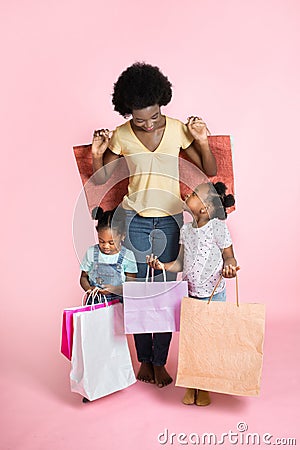 Beautiful young African mother and two litlle cute daughters in casual outfits, standing satisfied with shopping bags in Stock Photo