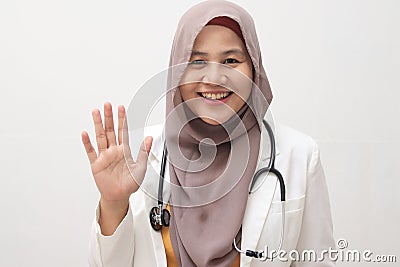 Beautiful young Asian muslim female doctor woman using stethoscope. Waving saying hello happy and smiling, friendly welcome Stock Photo