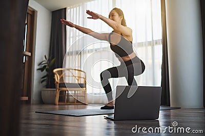 A beautiful young woman doing squats while watching online workout tutorials on laptop at home Stock Photo