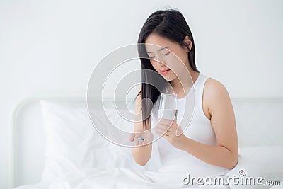 Beautiful young asian woman holding drug and glass of water while ill sitting on bed in the bedroom at home. Stock Photo