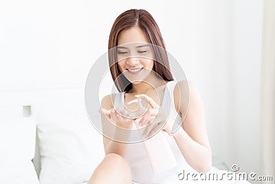 Beautiful Young Asian Woman pumping body lotion in hand on a white bed at home. Beauty and Body Care Concept Stock Photo