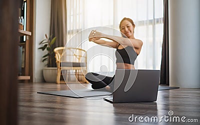 A beautiful young woman stretching arms while watching online workout tutorials on laptop at home Stock Photo