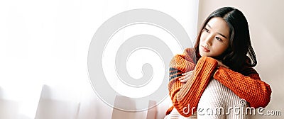 Beautiful young Asian woman wearing knitted warm sweater feeling depress sad girl lonely at home window thinking negative thoughts Stock Photo