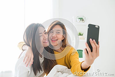 Beautiful young asian women LGBT lesbian happy couple sitting on bed hug and using phone taking selfie together bedroom at home. Stock Photo