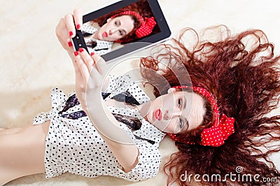 Beautiful young attractive woman pinup girl lying and taking selfy or selfie picture on digital tablet computer Stock Photo