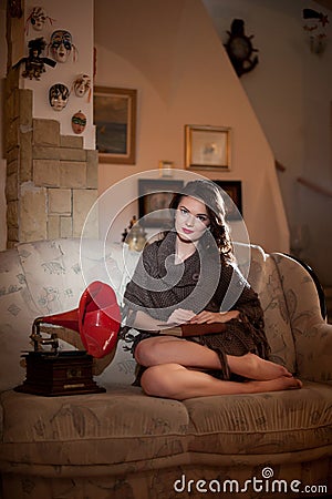 Beautiful young bare feet woman sitting on sofa holding a book having a red gramophone near her, vintage scenery Stock Photo