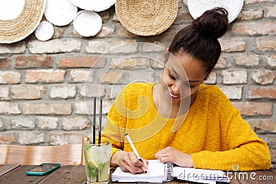 Beautiful young black woman writing notes at cafe Stock Photo